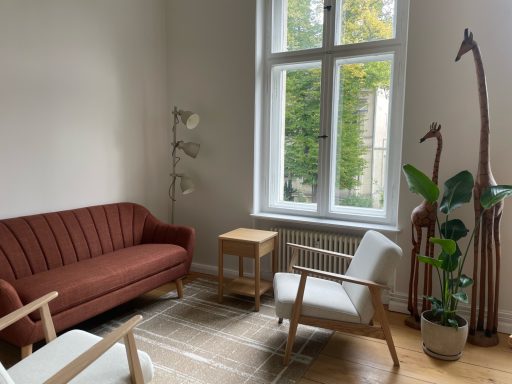 Heller Raum mit rotem Sofa, Holzstuhl, Beistelltisch und zwei Skulpturen von Giraffen.